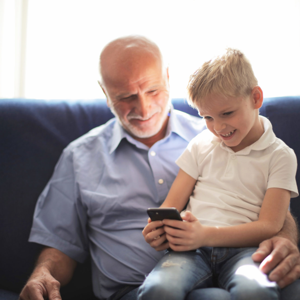 Child using phone while sitting on elderly adult's lap