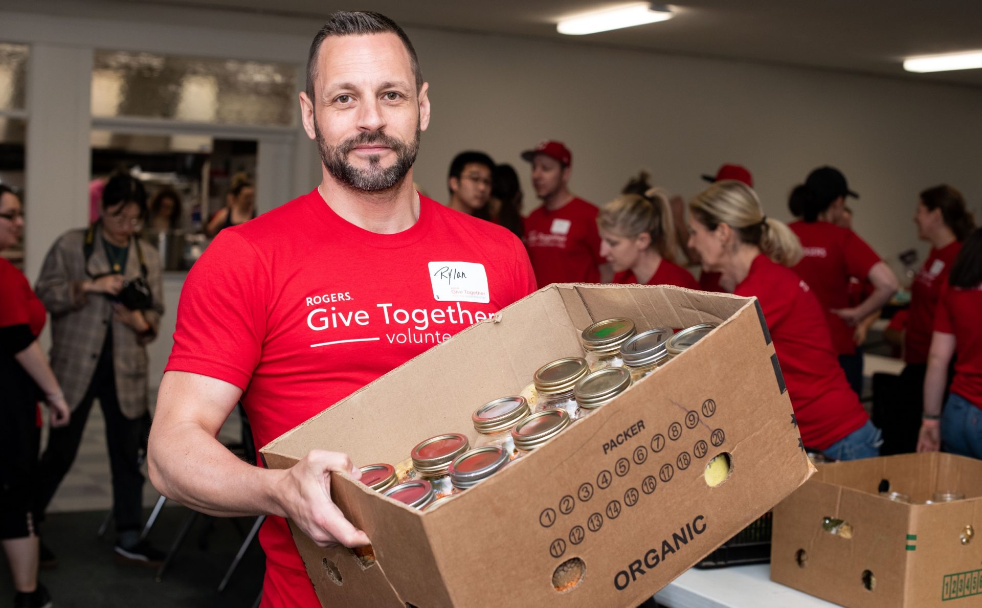 Rogers volunteer holding a box of canned foods inside office
