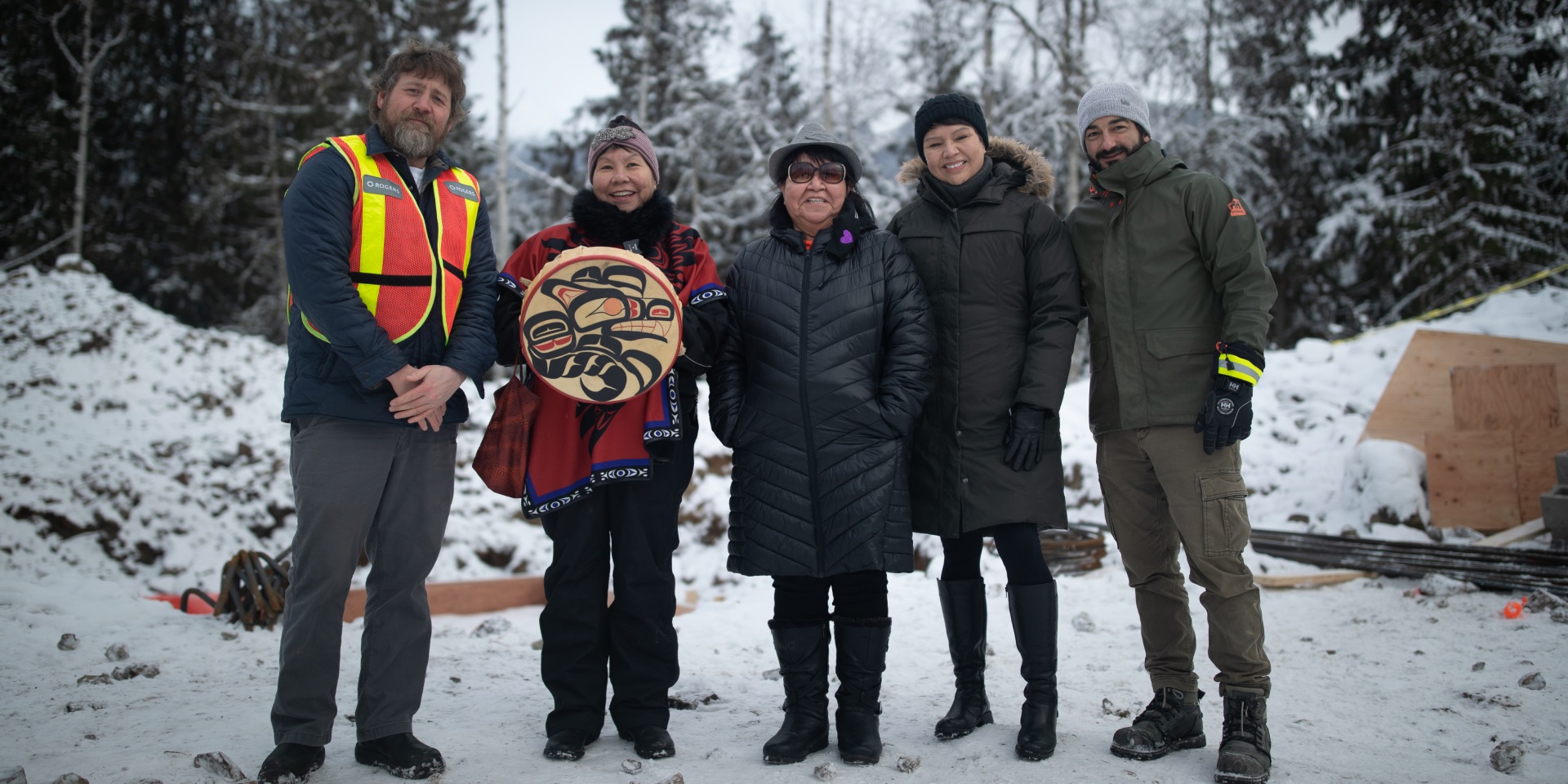 Group of people in snowy forest with one of them holding an Indigenous item
