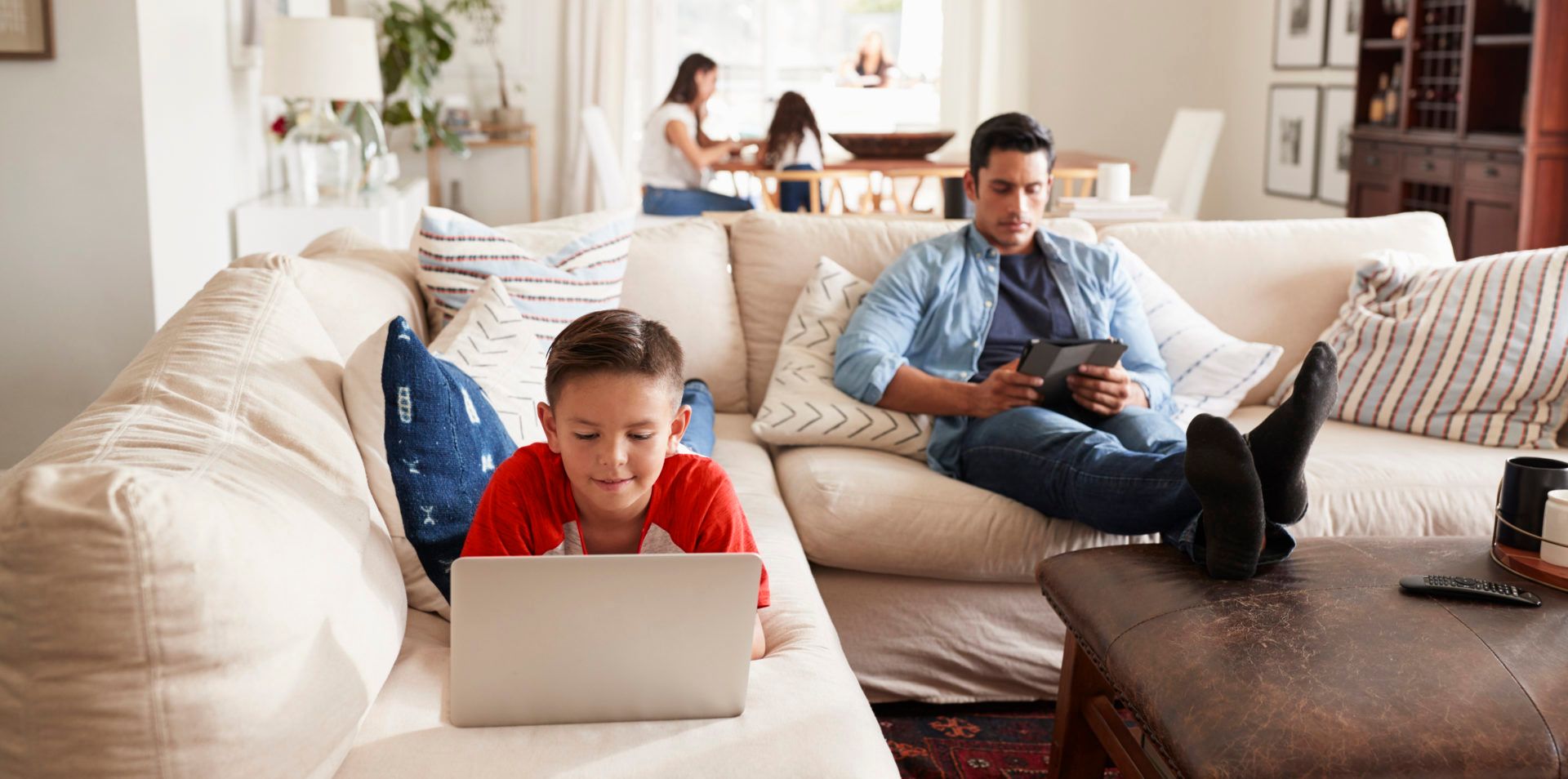 Child using laptop on couch while adult is looking at tablet