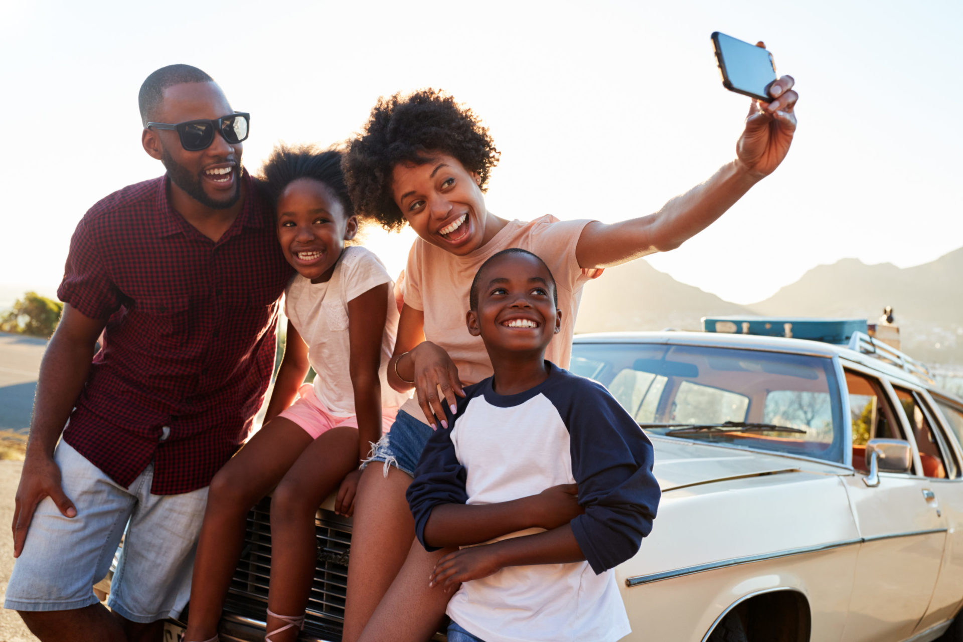 Happy family taking selfie while sitting on hood of car