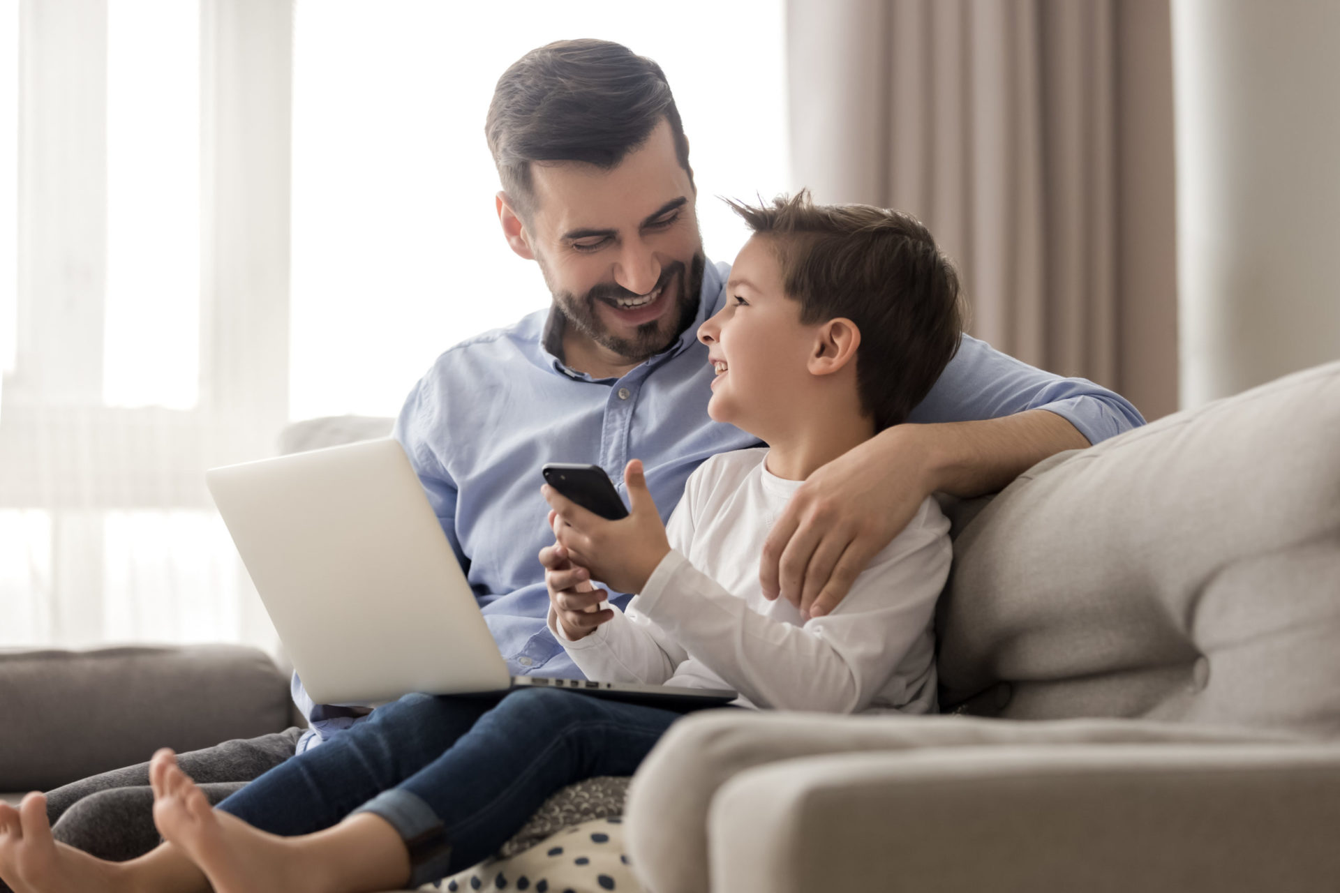 Adult and child on couch using laptop and phone