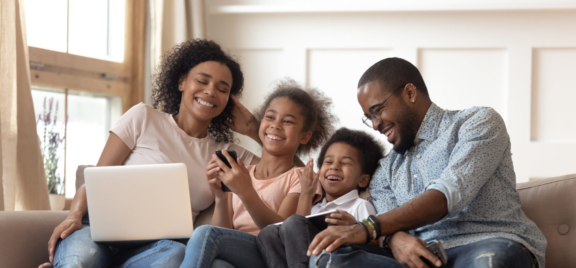 Happy family on couch using laptop, tablet, and smartphone