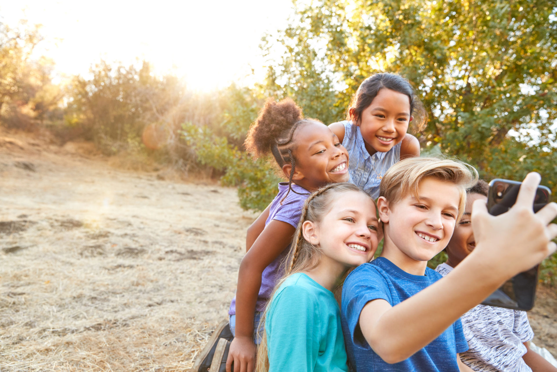 Group of five kids in sun outdoors taking selfie